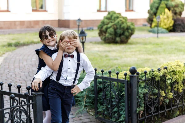 Cara loira bonito e menina bonito, tempo de diversão do ano letivo ao ar livre. Crianças vestidas com uniforme escolar brincam no parque — Fotografia de Stock