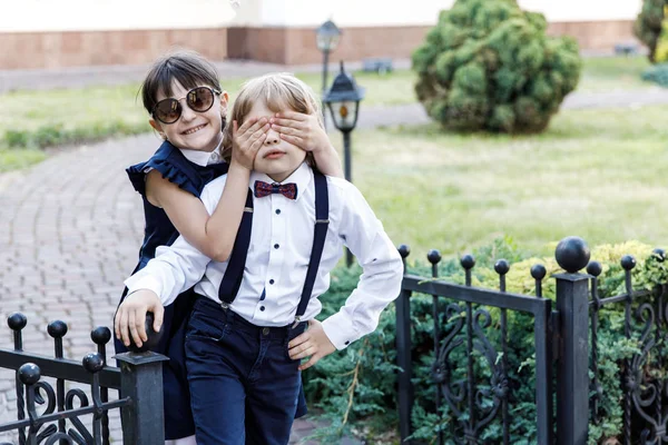 Cute blond guy and cute girl, school year fun time outdoors. Children dressed in school uniform play games in the park