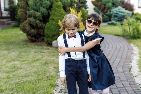 Cute blond guy and cute girl, school year fun time outdoors. Children dressed in school uniform play games in the park