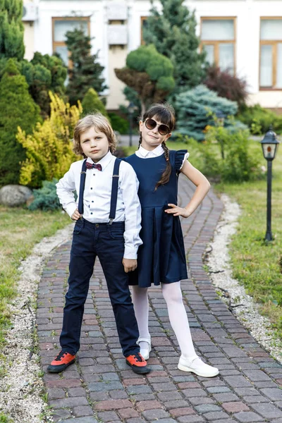 Cute blond guy and cute girl, school year fun time outdoors. Children dressed in school uniform play games in the park