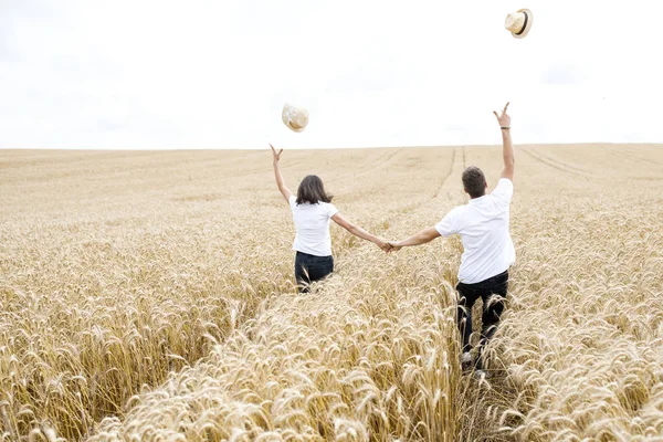 Красивая счастливая пара - парень и девушка веселятся на поле среди колосьев пшеницы, бегают и веселятся. Летние каникулы — стоковое фото
