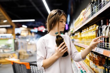 Genç güzel kız büyük bir mağazada alışveriş. Kız süpermarketten alışveriş yapıyor. Kız cam şişede yağ seçer