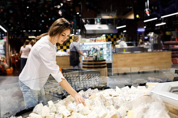 Genç güzel kız büyük bir mağazada alışveriş. Kız süpermarketten alışveriş yapıyor. Kız kaliteli ürünler seçer