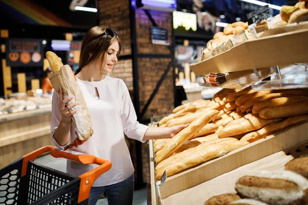 Genç güzel kız büyük bir mağazada alışveriş. Kız süpermarketten alışveriş yapıyor. Kız güzel kokulu bir pasta seçer