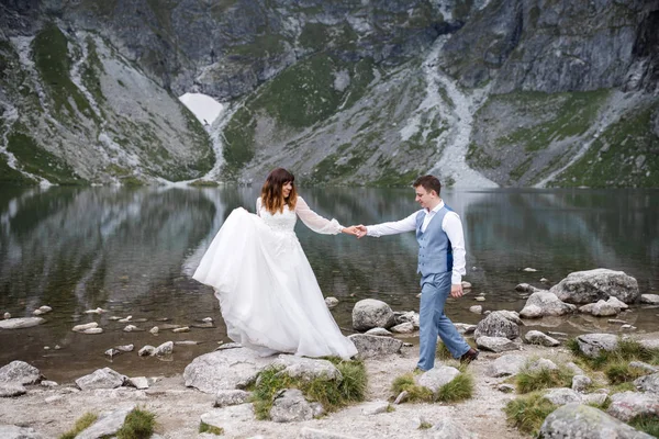 Aranyos fiatal szerelmesek töltenek időt a hegyekben, közel a tóhoz. Két friss házaspár sétál fel egyedül. Nászút. — Stock Fotó