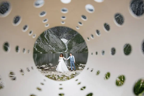 Söta unga kärleksfulla par tillbringar tid i bergen nära sjön. Ett par nygifta går fram ensam. Smekmånad — Stockfoto