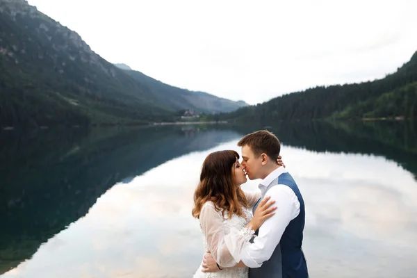 Aranyos fiatal szerelmesek töltenek időt a hegyekben, közel a tóhoz. Két friss házaspár sétál fel egyedül. Nászút. — Stock Fotó