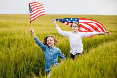 Bir adam ve kız ellerinde Amerikan bayrağıyla tarlada koşuyorlar.