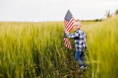 Yakışıklı sarışın bir çocuk elinde Amerikan bayrağıyla bir tarlada duruyor..