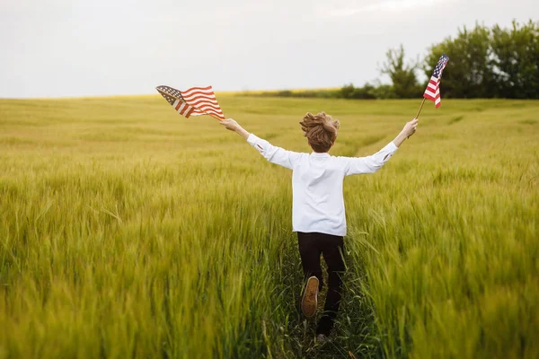 Boy runing with the american flag on the green wheat field celebrating national independence day. 4th of July concept. — Stock Photo, Image