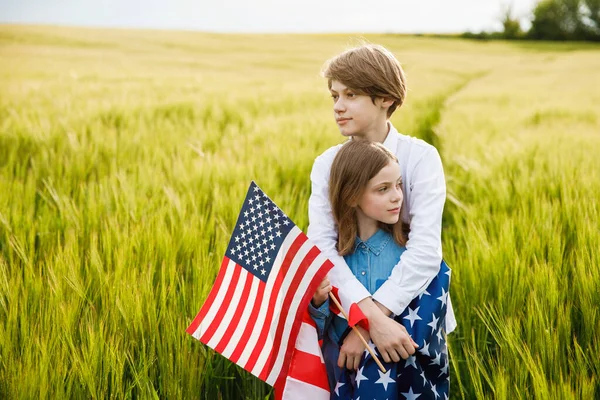 Поганий хлопець і дівчинка стоять на полі з американським прапором в руках. — стокове фото