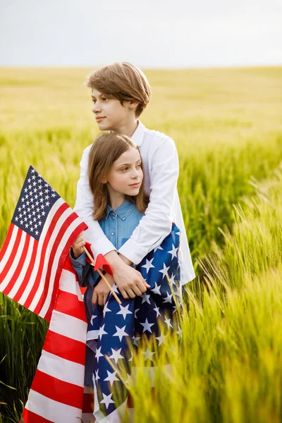Handsome guy and girl standing in a field with an American flag in their hands — Stock Photo, Image