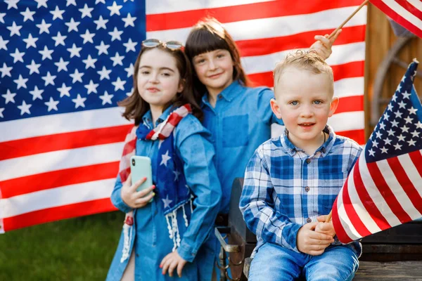 Tatlı sarışın oğlan ve iki kız Amerikan bayrağının arkasında sokakta eğleniyorlar.