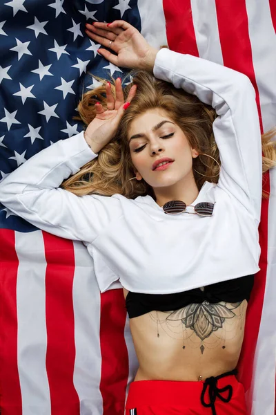 한 젊고 아름다운 소녀가 미국 국기 위에 누워 있다 — 스톡 사진