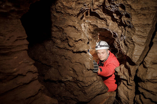 Man walking and exploring dark cave with light headlamp underground. Mysterious deep dark, explorer discovering mystery moody tunnel looking on rock wall inside.