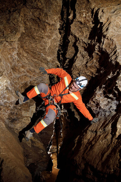 Speleologist descend by the rope in the deep vertical cave tunnel. Cave man hanging over abyss. View from the top og the tunnel.