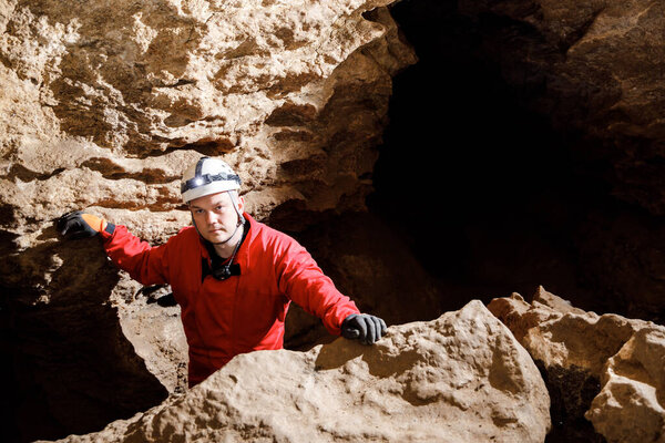 Man walking and exploring dark cave with light headlamp underground. Mysterious deep dark, explorer discovering mystery moody tunnel looking on rock wall inside.