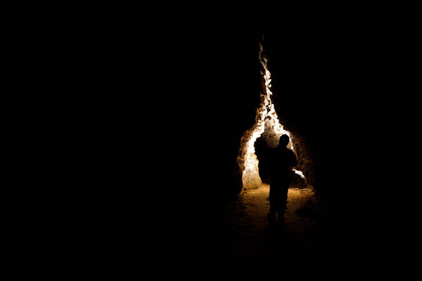 Man walking and exploring dark cave with light headlamp underground. Mysterious deep dark, explorer discovering mystery moody tunnel looking on rock wall inside.