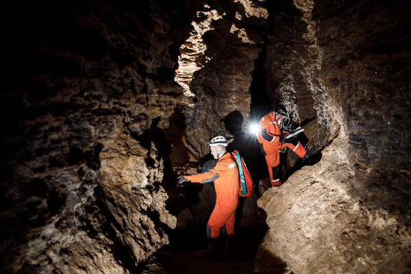 Two men, strong physique, explore the cave. Men dressed in special clothes to pass through the cave and stopped, looking at the map