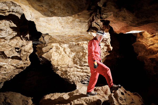 Man walking and exploring dark cave with light headlamp underground. Mysterious deep dark, explorer discovering mystery moody tunnel looking on rock wall inside.