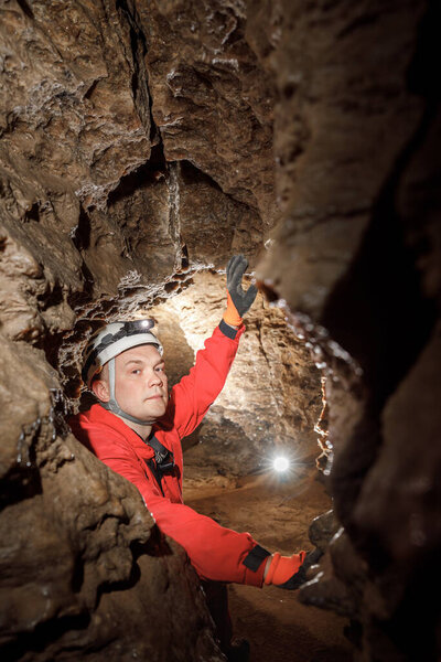 Man walking and exploring dark cave with light headlamp underground. Mysterious deep dark, explorer discovering mystery moody tunnel looking on rock wall inside.