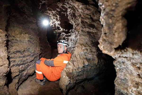 Man walking and exploring dark cave with light headlamp underground. Mysterious deep dark, explorer discovering mystery moody tunnel looking on rock wall inside.