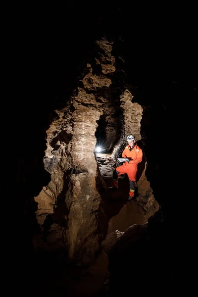 Man walking and exploring dark cave with light headlamp and map in his hand underground. Mysterious deep dark, explorer discovering mystery moody tunnel looking on rock wall inside. — Stock Photo, Image