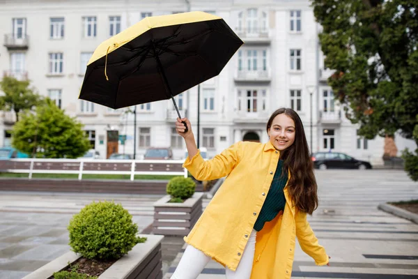 Una giovane ragazza adolescente cammina per la città con il tempo piovoso. La ragazza è vestita con vestiti colorati e stivali di gomma — Foto Stock