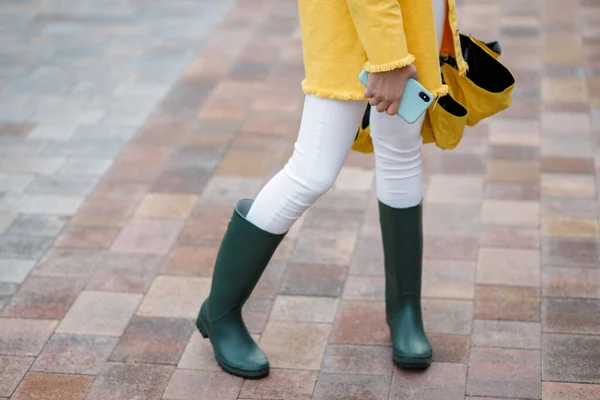 若い可愛い10代の少女が雨の日に街を歩いている。女の子は携帯電話を持っている色の服やゴム製のブーツに身を包んだ — ストック写真