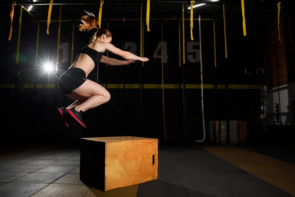 운동복을 입고 건강 체육관에서 크로스 핏 박스 위에서 점프하는 운동 선수 여자 — 스톡 사진