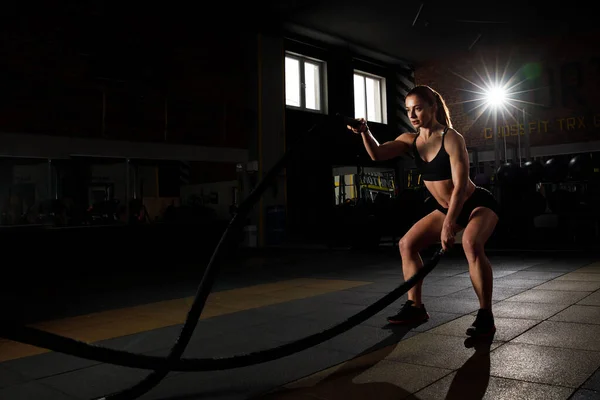 Powerful attractive muscular woman battle rope workout at the gym