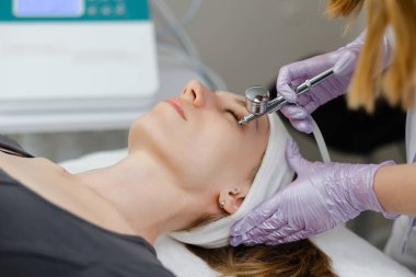 Güzellik uzmanı, cilt yenilenmesi ve su kaybı için müşterinin yüzüne serum uygulayan özel bir cihaz kullanıyor.