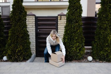 Müşteri, evinin ön kapısına bırakılan paketleri topluyor ve hızlı ve güvenilir teslimat hizmetinin keyfini çıkarıyor.