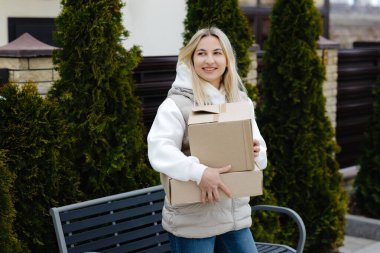 Mutlu müşteri online sipariş alıyor, gülümsüyor ve evinin önündeki bankın yanında karton kutular tutuyor.