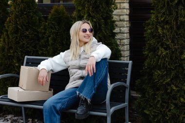 Modern evinin dışındaki bankta dinlenen şık bir kadın yanında paketler, huzur dolu bir anın tadını çıkarıyor.