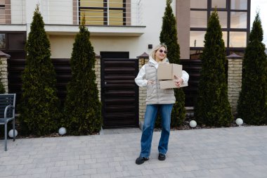 Genç kurye, neşeli bir müşteriye büyük bir paket teslim ediyor. Neşeli bir gülümsemeyle günü aydınlatıyor.