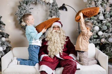 İki çocuk Noel Baba 'ya yastıklarla vuruyor Noel' de dekore edilmiş oturma odasında kanepede oynarken.