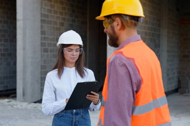 Erkek meslektaşımla inşaat planını tartışırken panoya not alan kadın mühendis.