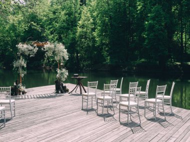 Romantik rustik düğün töreni Nehri yakınında. Beyaz ahşap sandalye ve çiçek arch.