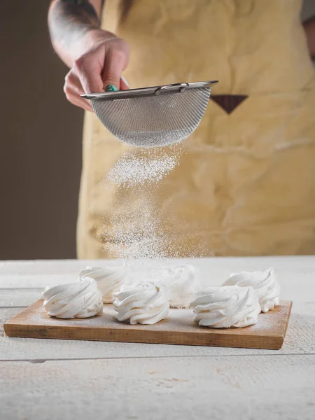 Kadın el tarafından pudra şekeri ile beyaz ev yapımı zephyr.