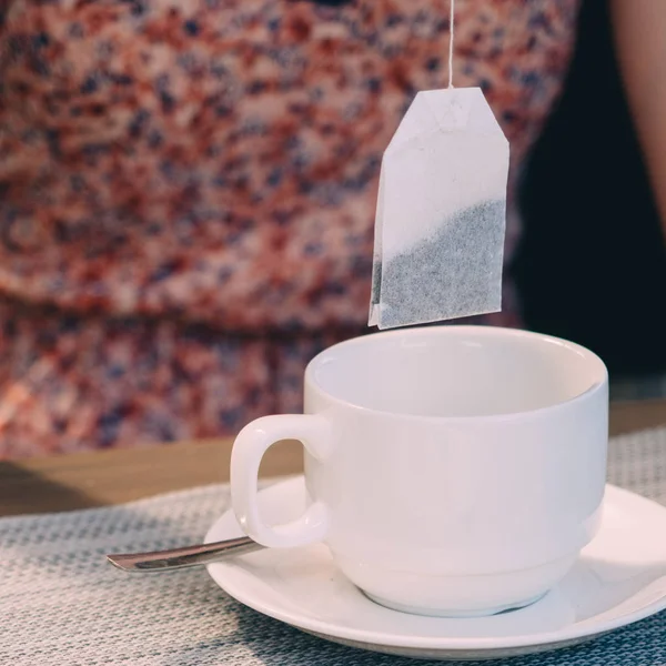 Tea bag over cup in cafe on wooden table.