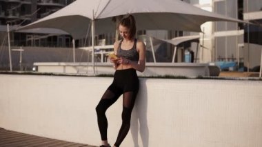 Cep telefonu üzerinde beyaz bir korkuluk eğilerek bakarak spor elbiseleri ince, çekici kız. Sahil. Rahatlatıcı, gülümseyen. Onun zaman zevk. Güneş parlıyor.