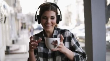 Kulaklık müzik dinlemek ve elinde bir fincan kahve ile dans eğlenceli, komik genç kız. Bulanık arka sokakta