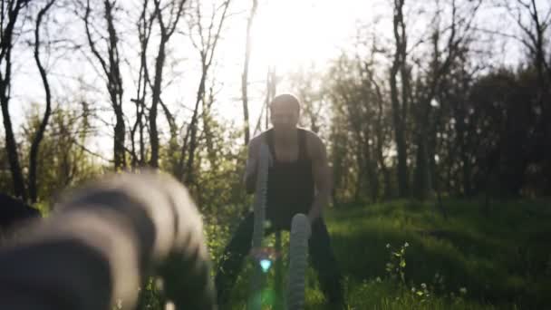 Muskulös man gör vågor med crossfit linor. Bosk, solen strålar på bakgrunden. Framifrån, närbild av linor — Stockvideo