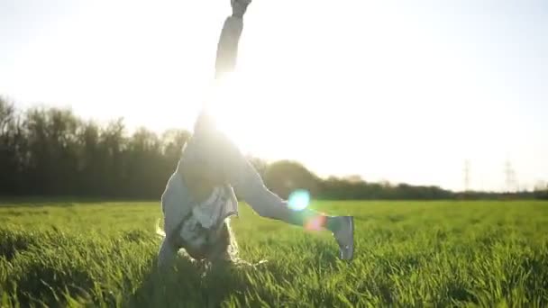 Vista frontal de una hermosa joven haciendo voltereta fuera en el campo verde. Disfruta de su tiempo. Día soleado. Sonriendo. Movimiento lento — Vídeos de Stock