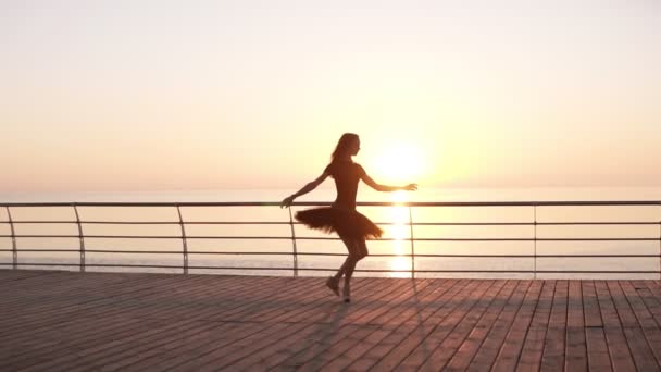 Молодая женщина в черной пачке занимается балетом на набережной. Боск. Солнечный свет. Привлекательная балерина практикует прыжки. Вид сбоку. Медленное движение — стоковое видео