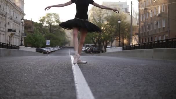 Балерина в черной балетной пачке и точка на пустой улице в середине дороги. Летнее утро. Молодая красивая женщина практикует балетные движения и упражнения. Закрывай. Без лица — стоковое видео