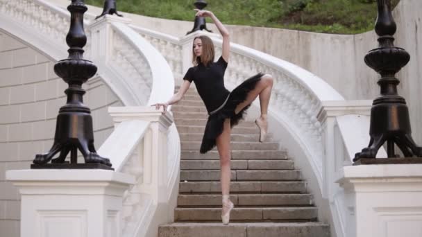 Lento movimiento de una joven rubia en tutú de pie en una hermosa escalera blanca fuera en la calle. Posando, practicando movimientos de ballet — Vídeos de Stock