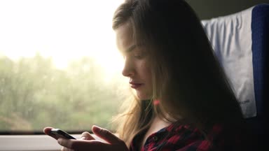 Uzun saçlı beyaz bir footafe kadar yakın kız rides bir trende. Oturma ve hareket eden telefon içinde sohbet. Konsantre andcalm. Yan görünüm