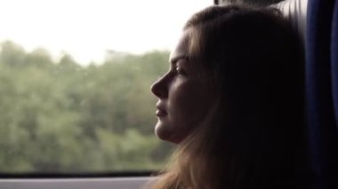 Rahat, uzun saçlı güzel kız hızlı tren sürme yan görünüm. Profil. Pencerenin oturuyor. Düşünceli, sakin kadın